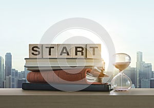 Wooden blocks with the word START, notebook, books and sand clock on table with panoramic city skyline background in the morning.