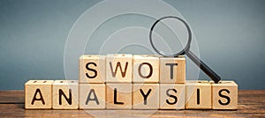 Wooden blocks with the word SWOT analysis and a magnifying glass. The method of strategic business planning. Strengths, weaknesses