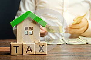 Wooden blocks with the word Tax, house with money in the hands of a businessman. The concept of paying tax for housing and