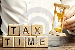 Wooden blocks with the word Tax time and taxpayer with a hourglass. The concept of paying the tax rate. Taxation / burden. Pay off photo