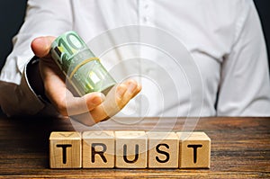 Wooden blocks with the word Trust and money in the hands of a businessman. Trust relationships between business partners, friends