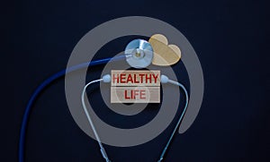 Wooden blocks with words `healthy life` and stethoscope on black background. Wooden heart. Medical and lifestyle concept