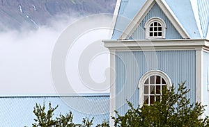 Wooden blue church in the mist, dwarfed by the mountain behind