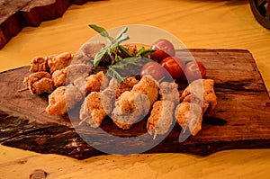 A wooden board with breaded chicken skewers, cherry tomatoes and sprigs of basil and rosemary photo