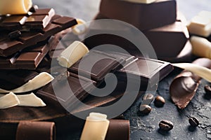 Wooden board with chocolate pieces on dark background