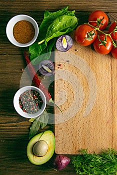 Wooden board with clear space. Around tomato and dill, olive oil, spice, peper, avocado, green onion, spinac and garlic. Top views