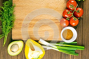 Wooden board with clear space. Around tomato and dill, olive oil, spice, peper, avocado, green onion, spinac and garlic. Top views