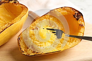 Wooden board with cooked spaghetti squash and fork on table