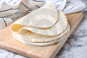 Wooden board with corn tortillas on marble table