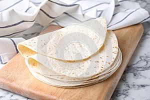 Wooden board with corn tortillas on marble table