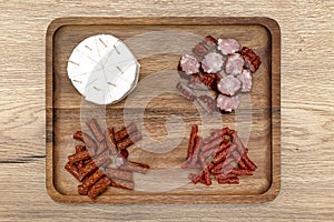 A wooden board with delicacies on which pieces of cheese and various types of meat lie, on the kitchen counter, top view.