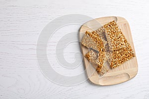 Wooden board with delicious kozinaki pieces on white table, top view. Space for text