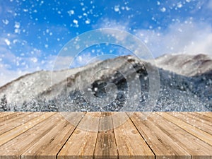 Wooden board empty table top on of blurred snowfall background. Perspective brown wood table over blur winter blue landscape.