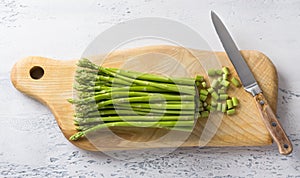 Wooden board of fresh asparagus with cut tough pieces and a knife on a light blue background, home cooking