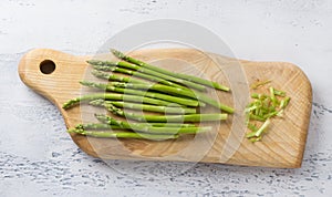 Wooden board of fresh asparagus with cut tough pieces on a light blue background, home cooking