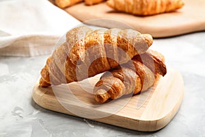 Wooden board with fresh croissants on grey table. French pastry