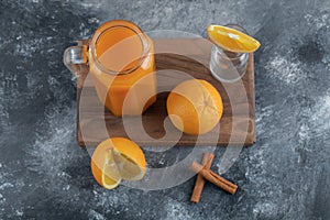 A wooden board with a glass jug of juice and orange fruits