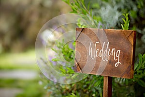 Wooden board with the inscription in paint Wedding. Sign for guests at the entrance, outdoors wedding ceremony decoration. Hand