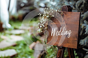 Wooden board with the inscription in paint Wedding. Sign for guests at the entrance, outdoors wedding ceremony decoration. Hand