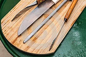 A wooden board with a knife, a pair of scissors, and a pair of tongs on it