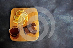 Wooden board with lemon, chocolate and a glass of cognac on a gray background