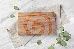 Wooden board on linen napkin on marble kitchen table with green leaf