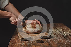 On wooden board man slicing fresh organic bread