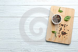 Wooden board with mixed pepper corns and basil leaves on white table. Space for text