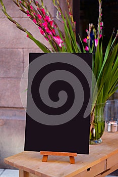 Wooden board for restaurant menu with empty space to add text standing at restaurant entrance with flower pot