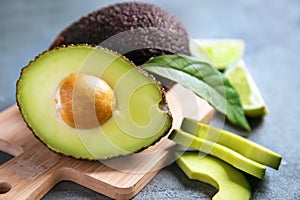 Wooden board with ripe avocados on grey textured background