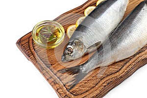 Wooden board with salted herrings, slices of lemon and oil on white background, closeup