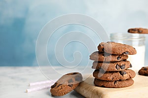 Wooden board with stack of tasty chocolate chip cookies on table.