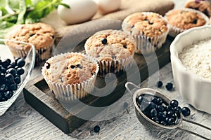 Wooden board with tasty blueberry muffins and fresh berries on table