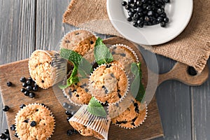 Wooden board with tasty blueberry muffins and fresh berries on table