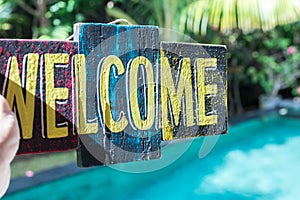 Wooden board with text welcome in man hand. Bali island. Welcome sign.