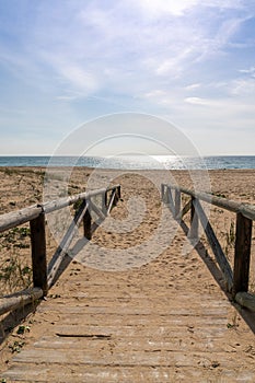 Wooden boardwalk and beach access leads directly onto beach with glistening calm ocean behind photo