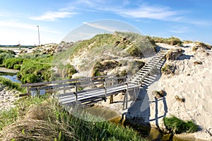 A wooden boardwalk bridge over a narrow stream to a small sand dune near Sola beach