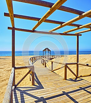 Wooden boardwalk going to a broad beach of fine sand dunes on a sunny day