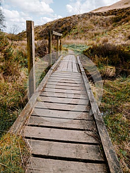Wooden boardwalk over muddy swampy boggy ground in the UK country side at Rivington Pike .