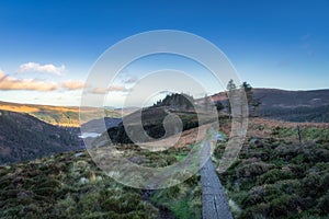 Wooden boardwalk on the top of a mountain with a view on Glendalough lakes and forest. Wicklow Mountains, Ireland