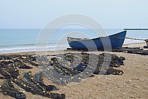 Wooden boat bordered on the beach next to fishing nets.