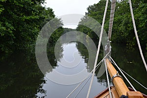 Wooden boat bow, bowsprit and rigging only quietly on a tranquil, tree lined river