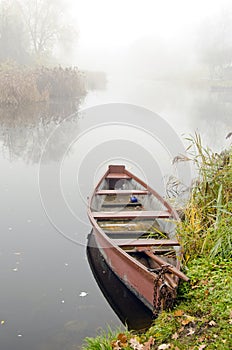 Wooden boat on coast of river sunken in dense fog.