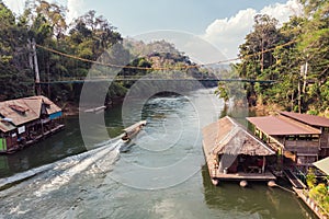 Wooden boat sailing on river kwai with tropical wooden village