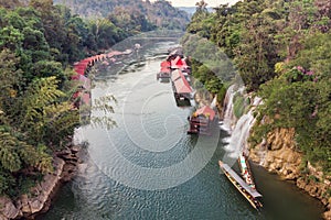 Wooden boat sailing river kwai with waterfall in tropical rainforest