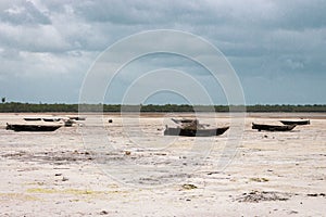 Wooden boats on low tide, toned. Zanzibar beach with old nautical vessel. African seascape with cloudy sky. Empty coast of ocean.
