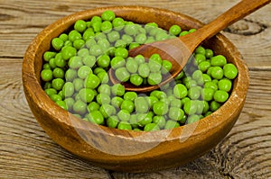 Wooden bowl with canned green peas on table