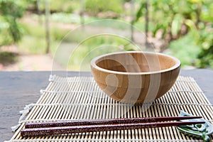 Wooden bowl with chopsticks on bamboo mat on wooden table in the garden