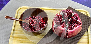 Wooden bowl containing wooden spoon and red pomegranate seeds. Pomegranate fruit open divided into five parts held together on a