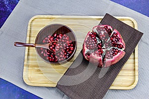 Wooden bowl containing wooden spoon and red pomegranate seeds. Pomegranate fruit open divided into five parts held together on a